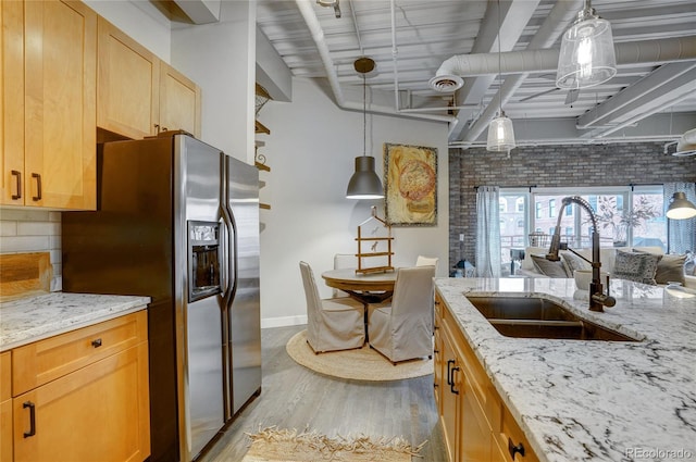 kitchen featuring light stone countertops, backsplash, stainless steel refrigerator with ice dispenser, and a sink