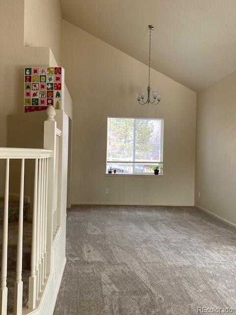 spare room with carpet, high vaulted ceiling, and an inviting chandelier