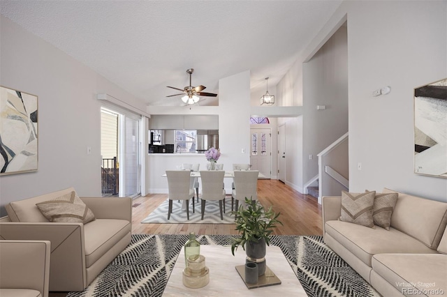 living room featuring ceiling fan, vaulted ceiling, a textured ceiling, and light wood-type flooring