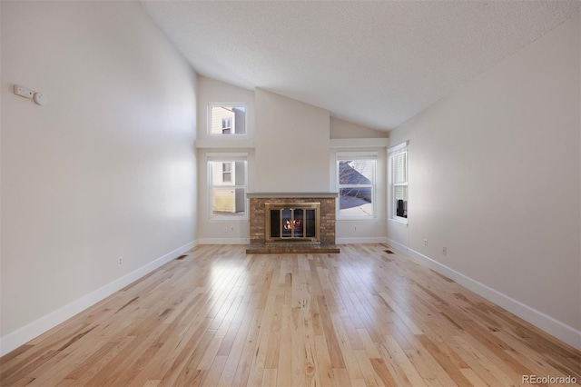 unfurnished living room with a brick fireplace, high vaulted ceiling, a textured ceiling, and light wood-type flooring