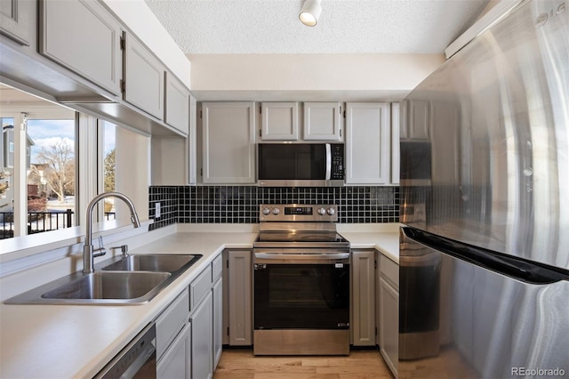 kitchen with sink, light hardwood / wood-style flooring, appliances with stainless steel finishes, tasteful backsplash, and a textured ceiling