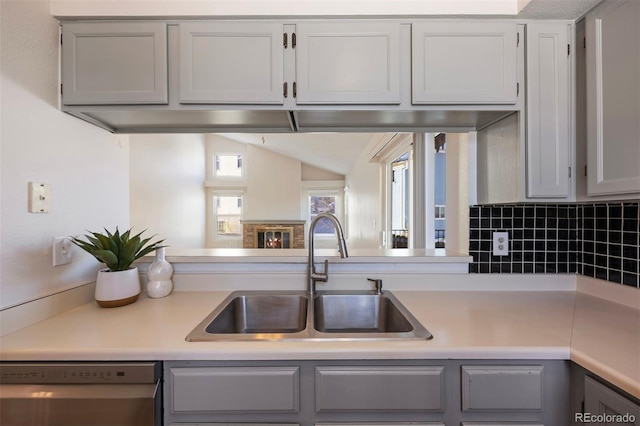 kitchen featuring sink, tasteful backsplash, stainless steel dishwasher, gray cabinets, and a fireplace