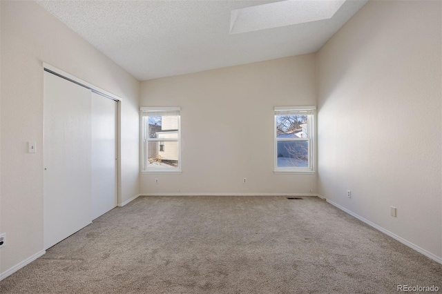 unfurnished bedroom featuring lofted ceiling with skylight, light carpet, a textured ceiling, and a closet