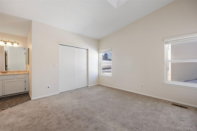 unfurnished bedroom with vaulted ceiling, connected bathroom, sink, light colored carpet, and a closet