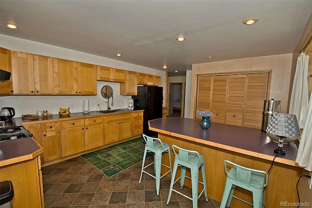 kitchen featuring black refrigerator, sink, gas stovetop, and a kitchen bar