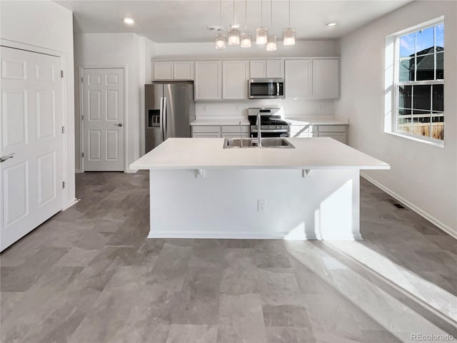 kitchen with a kitchen island with sink, appliances with stainless steel finishes, light countertops, and a sink