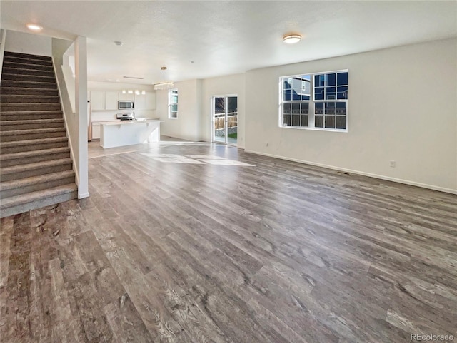 unfurnished living room featuring stairs, baseboards, and wood finished floors