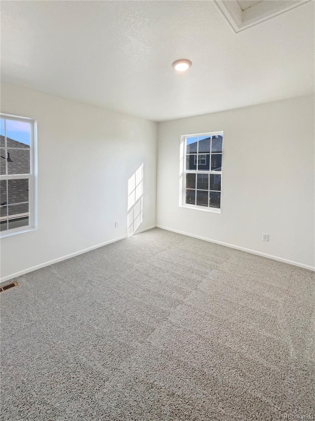 empty room with carpet, visible vents, and baseboards