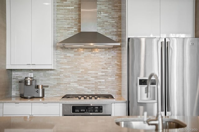 kitchen with appliances with stainless steel finishes, tasteful backsplash, white cabinetry, light stone countertops, and wall chimney range hood