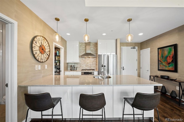 kitchen with pendant lighting, stainless steel refrigerator with ice dispenser, white cabinets, kitchen peninsula, and wall chimney exhaust hood