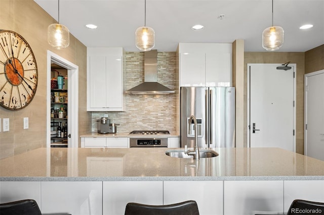 kitchen featuring pendant lighting, white cabinets, appliances with stainless steel finishes, and wall chimney range hood