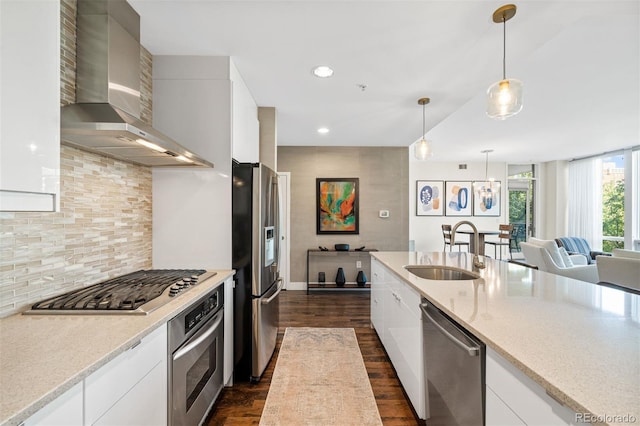 kitchen featuring appliances with stainless steel finishes, white cabinetry, sink, hanging light fixtures, and wall chimney exhaust hood