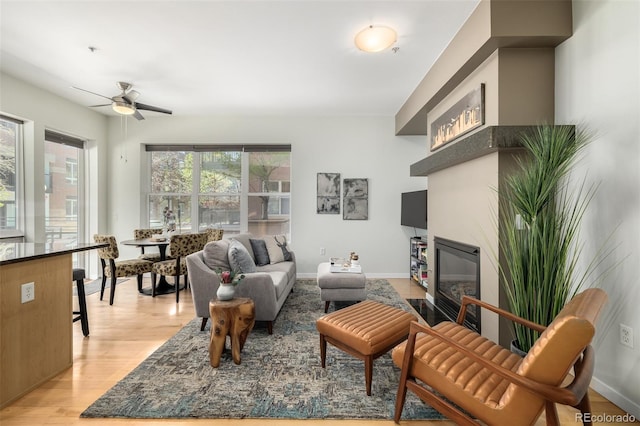 living room featuring light wood-style floors, a fireplace with flush hearth, baseboards, and a ceiling fan