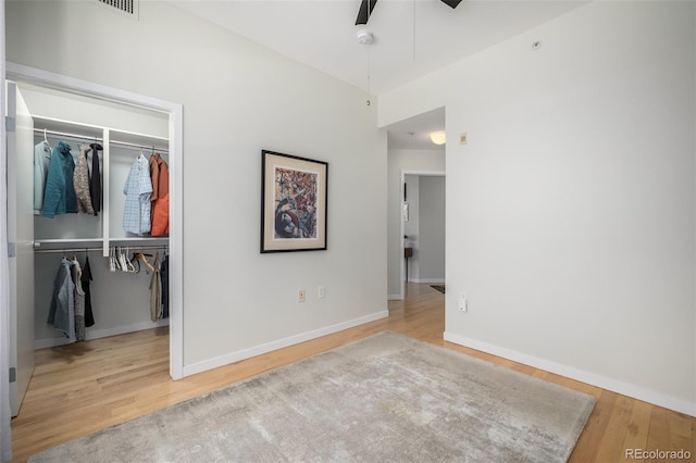 unfurnished bedroom featuring a walk in closet, a closet, a ceiling fan, wood finished floors, and baseboards