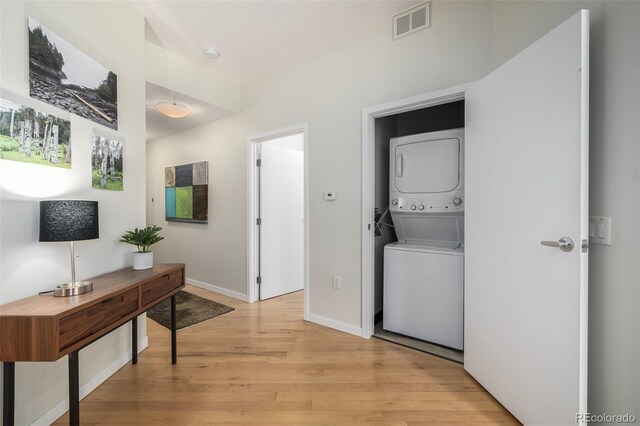 laundry room with light wood-type flooring and stacked washer / dryer