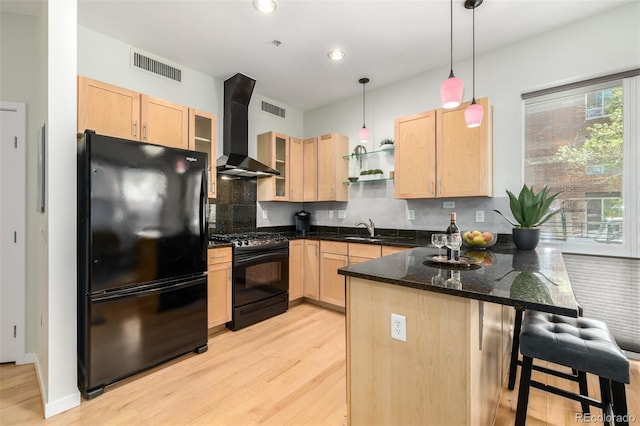 kitchen with wall chimney range hood, light brown cabinets, hanging light fixtures, and black appliances