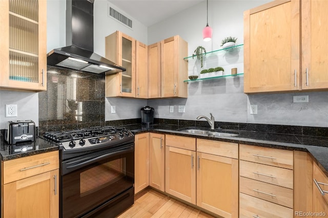 kitchen featuring black range with gas cooktop, glass insert cabinets, wall chimney range hood, pendant lighting, and a sink