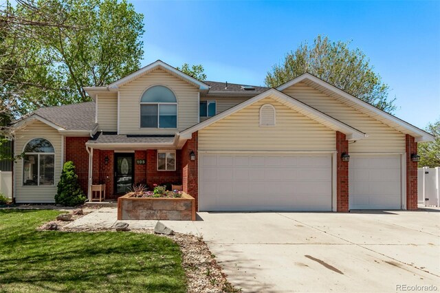 traditional-style home with brick siding, an attached garage, driveway, a shingled roof, and a front lawn