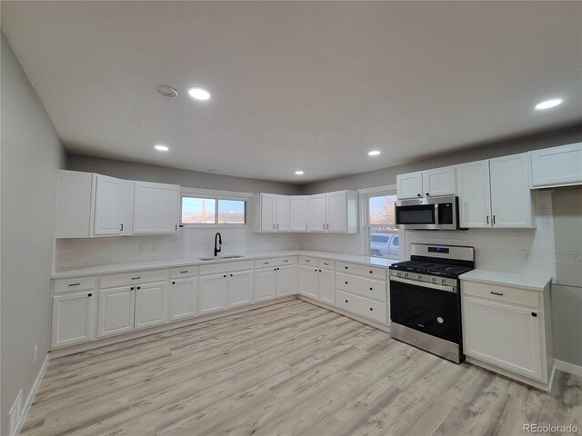 kitchen with a sink, stainless steel appliances, white cabinets, and light wood finished floors