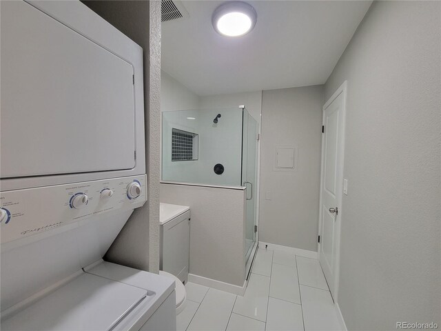 clothes washing area featuring laundry area, light tile patterned floors, baseboards, and stacked washer / drying machine
