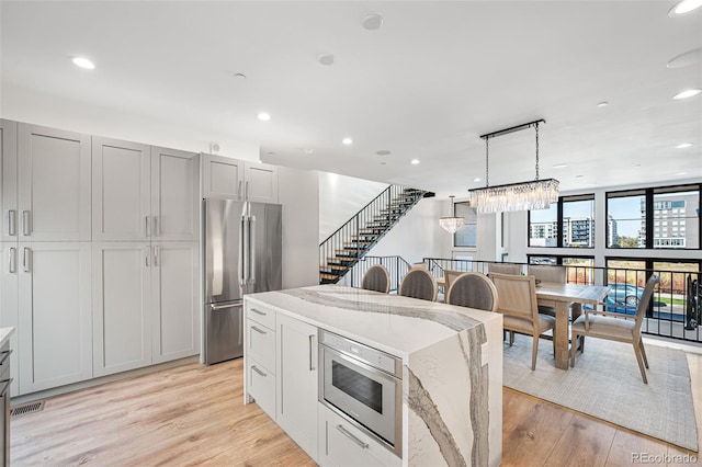 kitchen with light stone counters, recessed lighting, high end refrigerator, a center island, and light wood finished floors