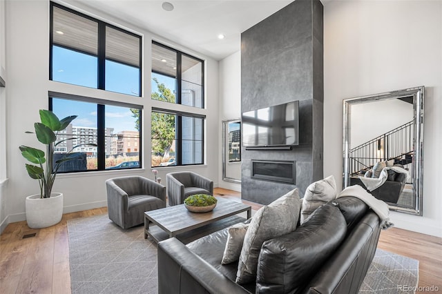 living area with light wood finished floors, a high ceiling, a high end fireplace, and baseboards