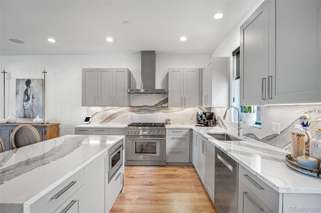 kitchen featuring wall chimney range hood, a sink, appliances with stainless steel finishes, and gray cabinetry