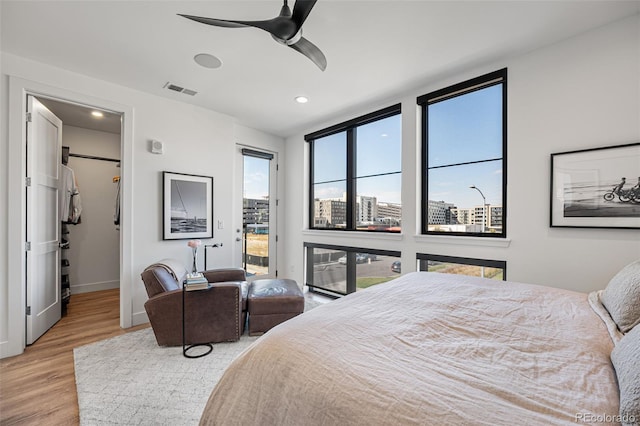 bedroom with a city view, wood finished floors, a ceiling fan, visible vents, and access to exterior