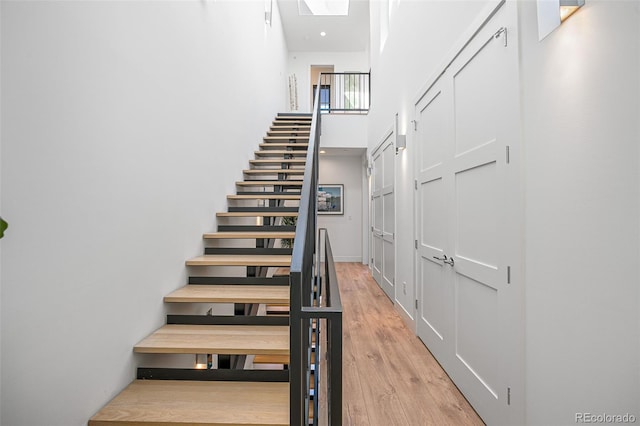 stairs with a skylight, wood finished floors, and a towering ceiling