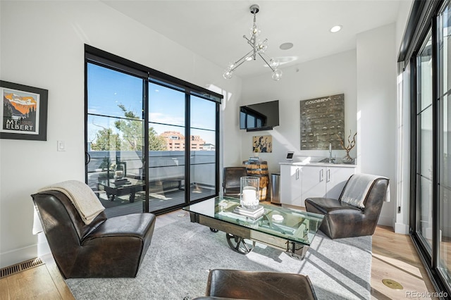 living room featuring light wood-style flooring, visible vents, baseboards, and a chandelier