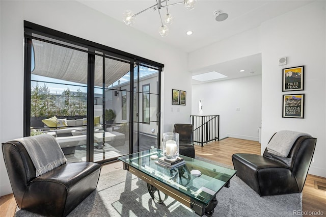 living room featuring a skylight, a notable chandelier, baseboards, and wood finished floors