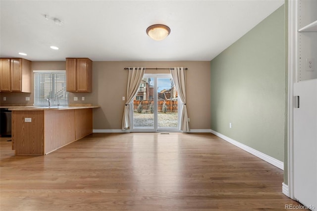 kitchen with black dishwasher, kitchen peninsula, light hardwood / wood-style flooring, and sink