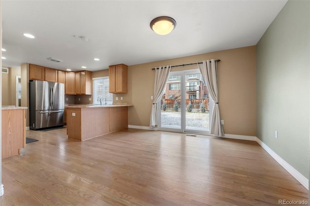 kitchen with kitchen peninsula, stainless steel fridge, light hardwood / wood-style flooring, and sink