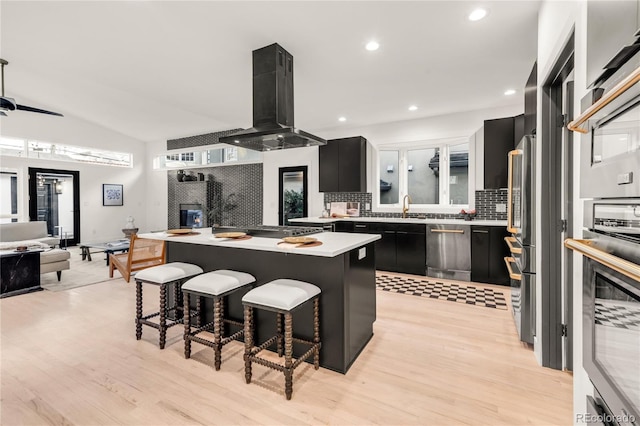 kitchen featuring lofted ceiling, a breakfast bar, appliances with stainless steel finishes, island range hood, and a kitchen island