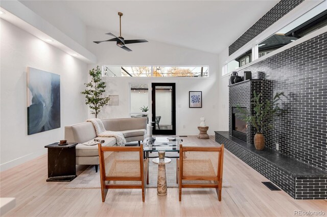 living room featuring a tiled fireplace, ceiling fan, hardwood / wood-style flooring, and high vaulted ceiling