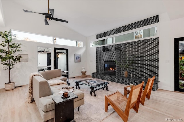 living room featuring ceiling fan, high vaulted ceiling, light wood-type flooring, and a fireplace