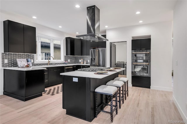 kitchen with light hardwood / wood-style flooring, appliances with stainless steel finishes, a kitchen island, island range hood, and a kitchen bar