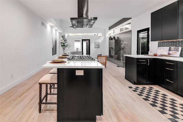 kitchen with a breakfast bar area, island range hood, a center island, stainless steel gas stovetop, and light hardwood / wood-style floors