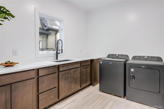 washroom with sink, washer and clothes dryer, light hardwood / wood-style floors, and cabinets