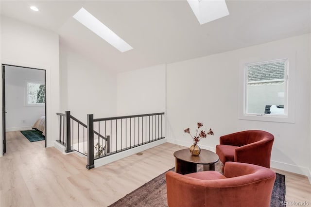 sitting room featuring lofted ceiling with skylight and light hardwood / wood-style flooring