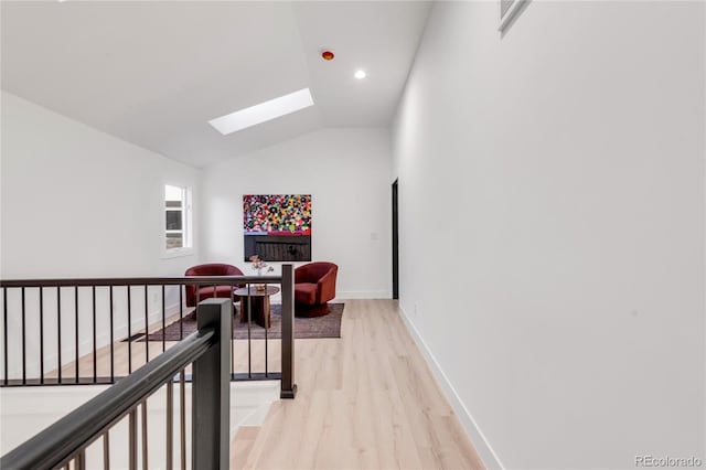 hallway featuring vaulted ceiling with skylight and light wood-type flooring