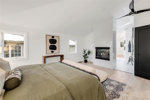 bedroom with a multi sided fireplace, vaulted ceiling, and light hardwood / wood-style floors