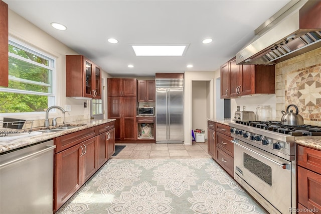 kitchen featuring high quality appliances, light stone countertops, custom range hood, decorative backsplash, and sink