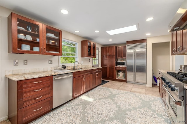 kitchen featuring sink, light stone counters, premium appliances, and range hood