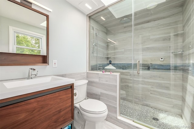 bathroom with tile walls, vanity, toilet, and a shower with shower door