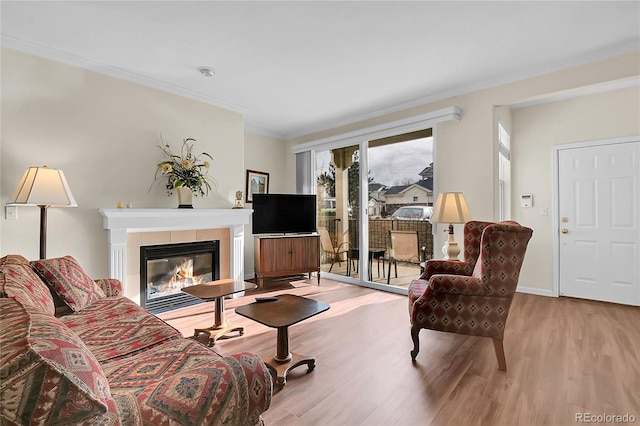 living room with a tile fireplace, light hardwood / wood-style flooring, and ornamental molding