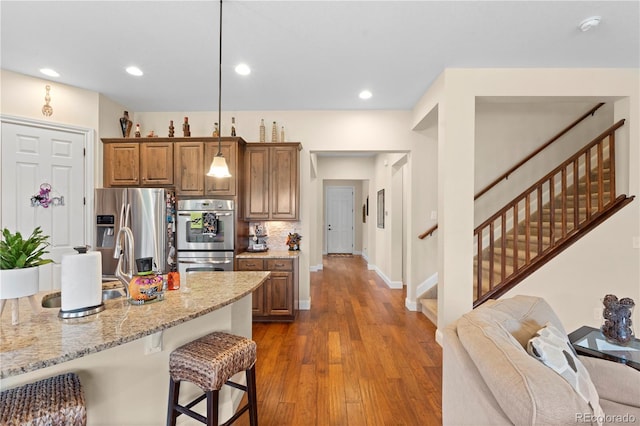 15003 W 63rd Ave, Arvada, CO 80403 - kitchen featuring stainless steel appliances, a breakfast bar, brown cabinets, light stone counters, and backsplash