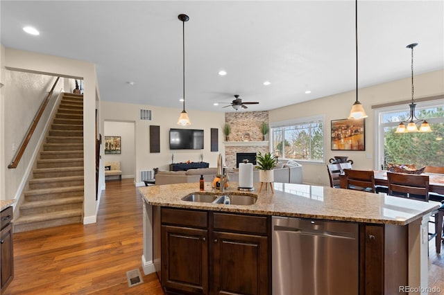 15003 W 63rd Ave, Arvada, CO 80403 - kitchen featuring stainless steel dishwasher, a fireplace, ceiling fan, a center island with sink, and dark brown cabinets