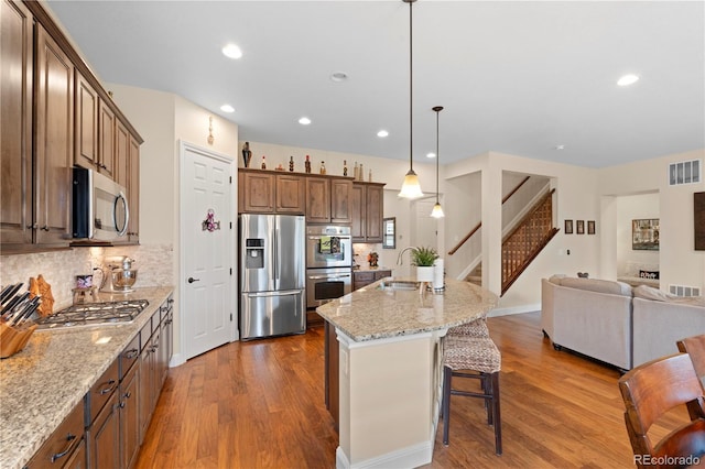 15003 W 63rd Ave, Arvada, CO 80403 - kitchen featuring stainless steel appliances, open floor plan, dark wood-style flooring, a kitchen breakfast bar, and light stone countertops