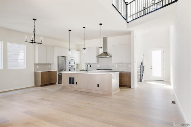 11324 Alla Breve Cir, Lone Tree, CO 80134 - kitchen with modern cabinets, wall chimney range hood, black stovetop, a chandelier, and light wood-style floors